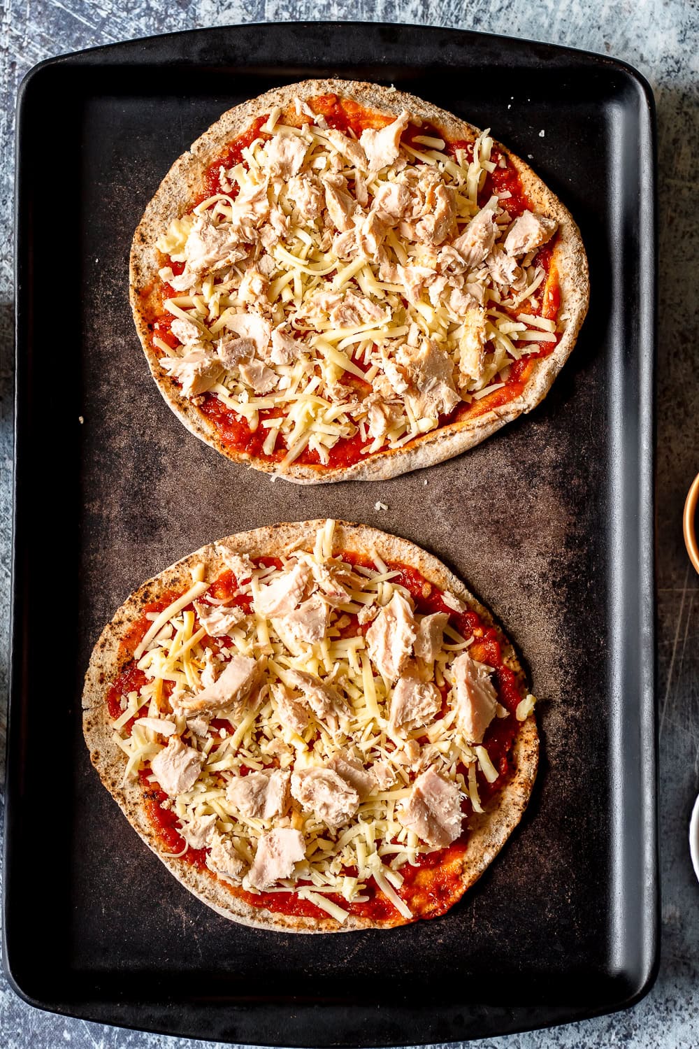 a process photo showing the tuna added to the pitas with pizza sauce and cheese
