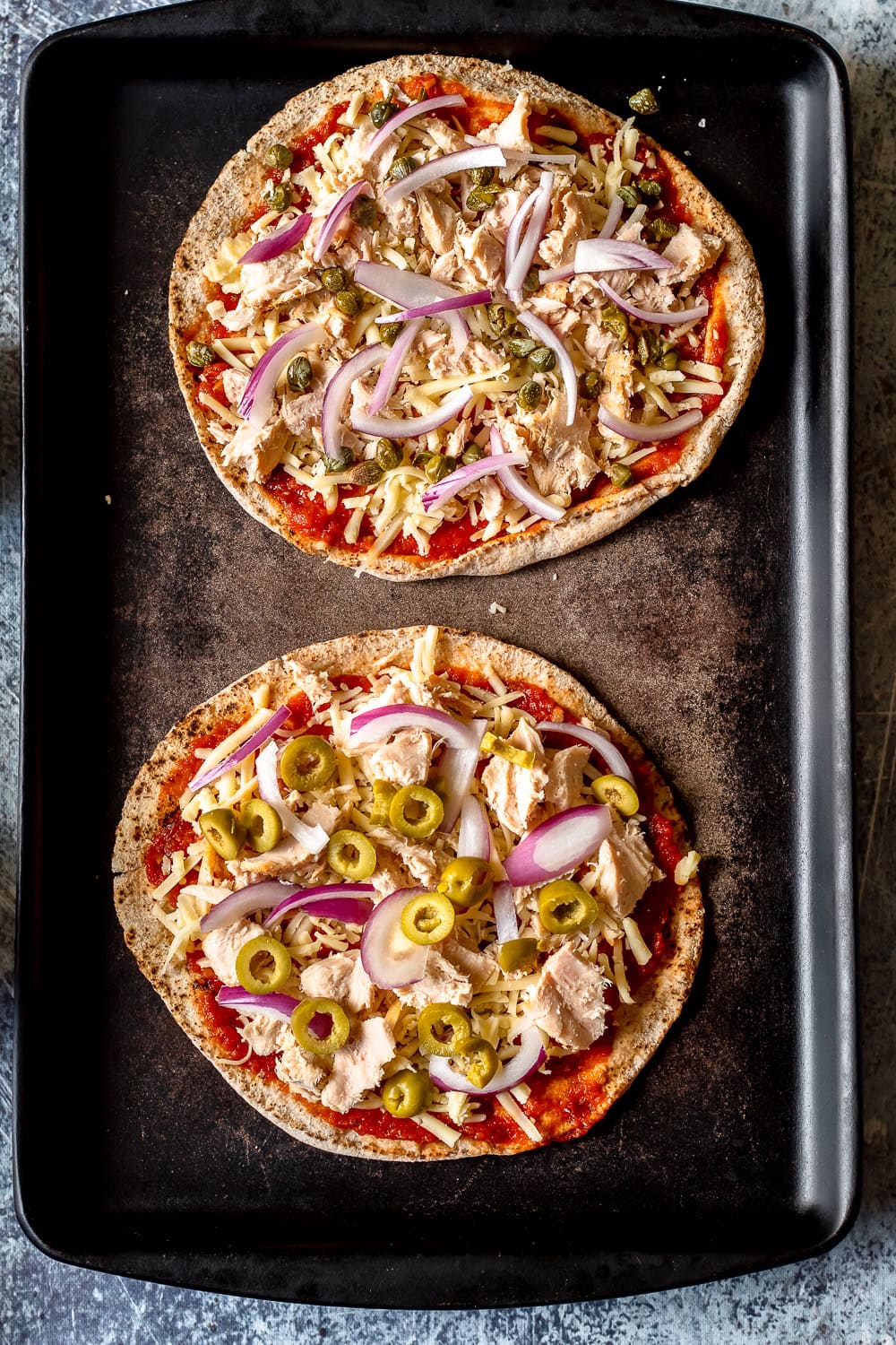 a process photo showing the olives, red onion, and capers added to the pita pizzas