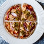 close up, overhead view of a pizza with tuna, olives, red onion, and cheese on a white plate against a dark backdrop
