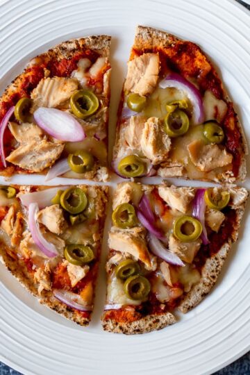 close up, overhead view of a pizza with tuna, olives, red onion, and cheese on a white plate against a dark backdrop