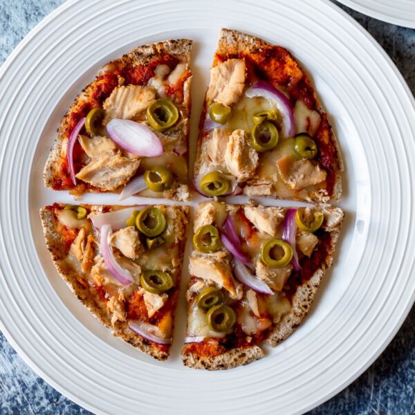close up, overhead view of a pizza with tuna, olives, red onion, and cheese on a white plate against a dark backdrop